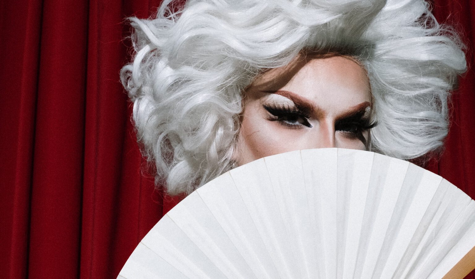 Een drag queen die met een waaier zwaait die ze gekocht heeft in de eerste dragwinkel van Nederland