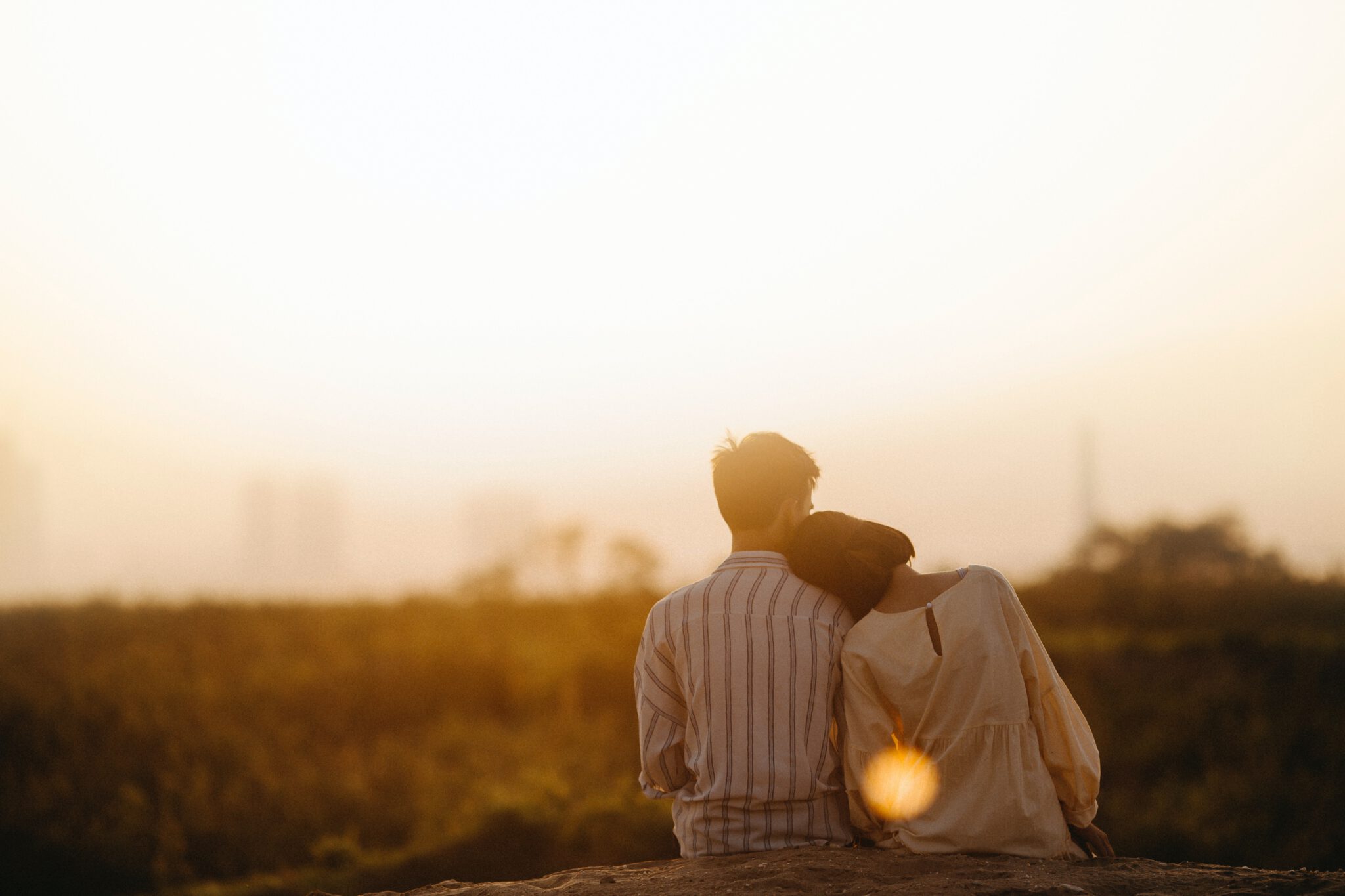 Vrouw zit met hoofd op schouder van haar vriend bij zonsondergang