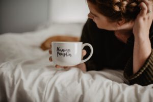 Vrouw die op bed ligt met kopje in haar hand