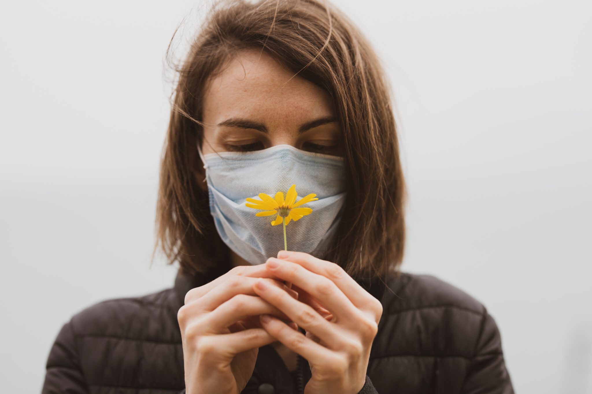 vrouw houdt bloem voor haar neus met mondkap op